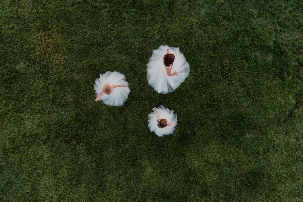 three flower girls twirl dresses as drone captures portrait from above.
