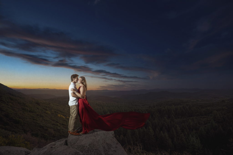 couple atop rock as sun sets.