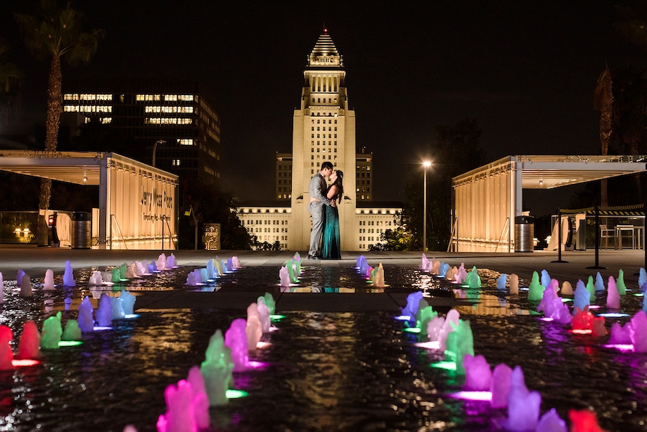 couple in front of building with small, colored fountains in front of them.