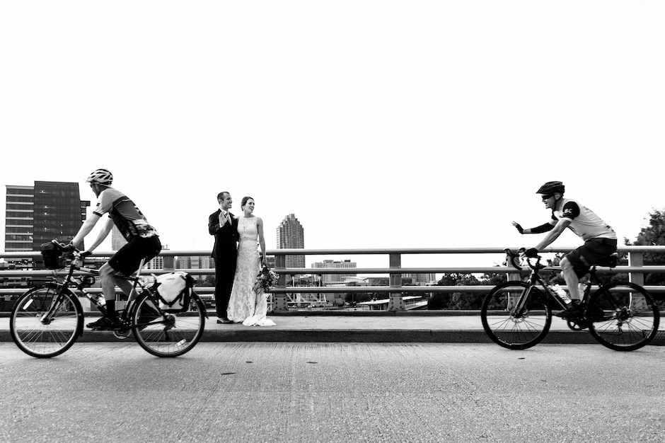 bride and groom on bridge, with bicyclists in foreground.